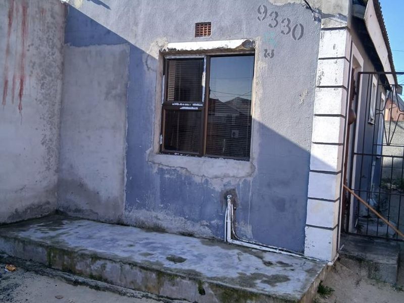 Front exterior view of a residential property showing a concrete porch, aluminium window, and weathered wall finishes requiring maintenance.