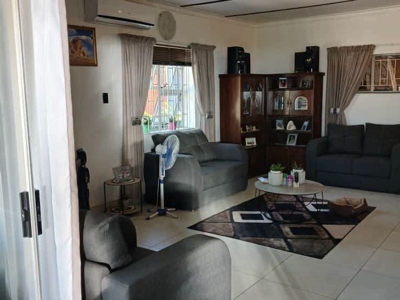 A comfortable living room featuring tiled flooring, an exposed beam ceiling, and a split-system air conditioner, with access via a sliding glass door.