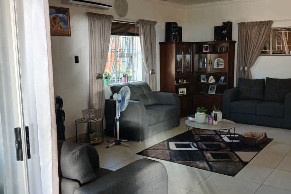 A comfortable living room featuring tiled flooring, an exposed beam ceiling, and a split-system air conditioner, with access via a sliding glass door.