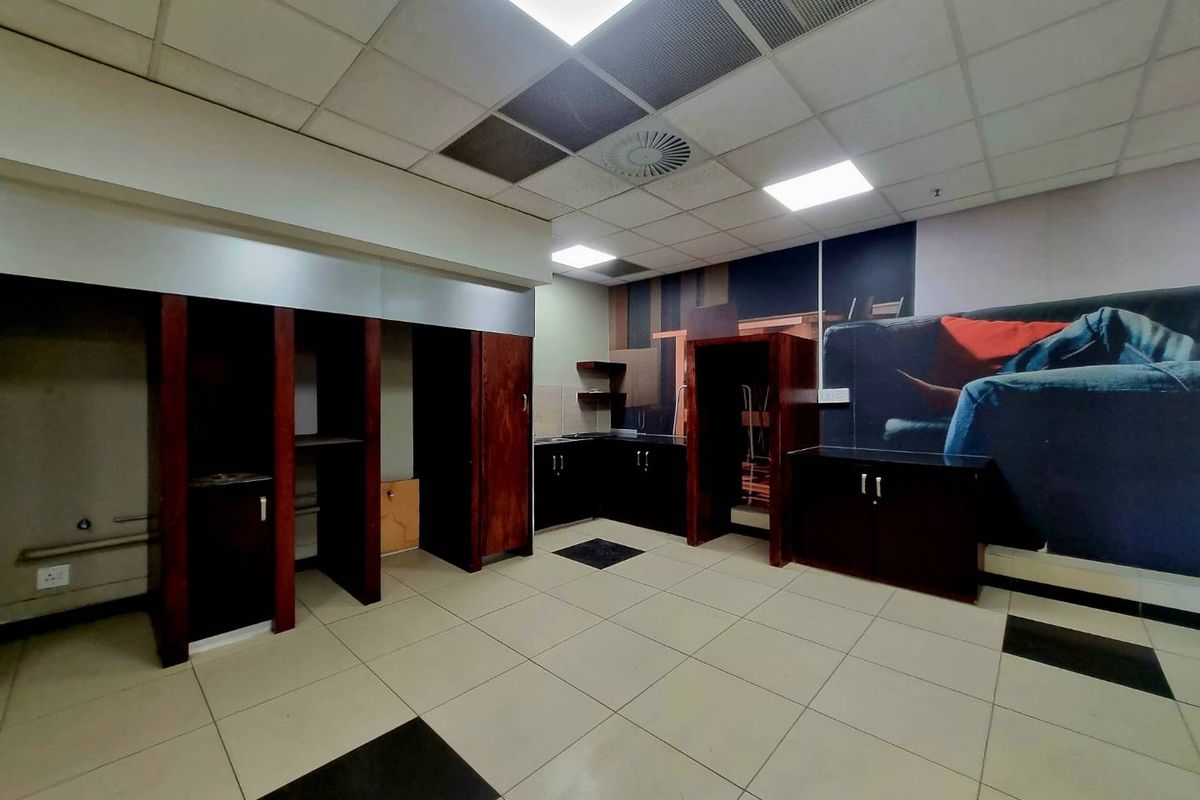 An industrial-style kitchen area featuring built-in dark wood cabinetry, tiled flooring, and a suspended ceiling with recessed lighting, currently in a vacant state.