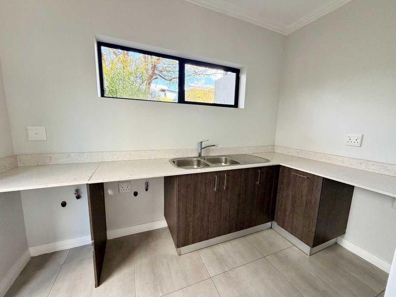 A clean and modern scullery featuring dark wood cabinetry, stone countertops, a double bowl sink, and neutral tiled flooring.