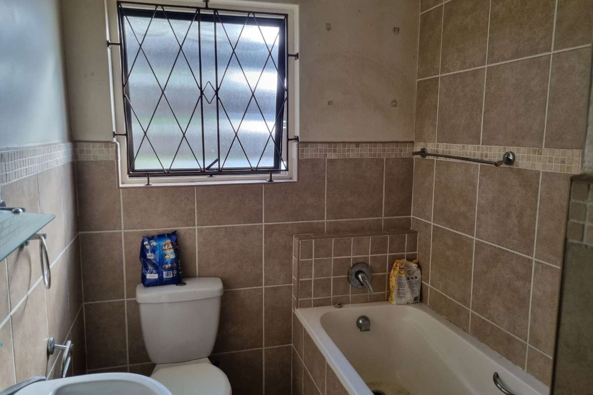 A dated bathroom featuring a bathtub, toilet, and basin with tiled walls and a security-barred window.