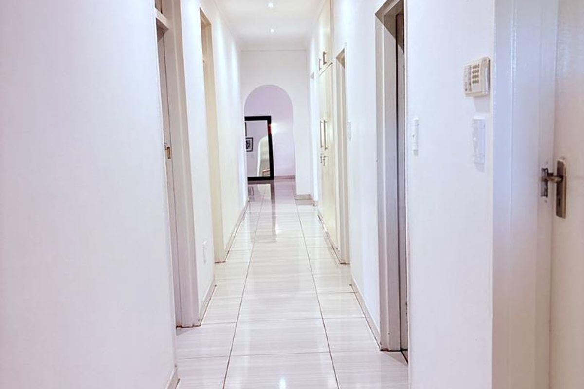 A bright, clean hallway featuring neutral tiled flooring, recessed downlighting, and built-in storage cupboards, providing access to multiple rooms.