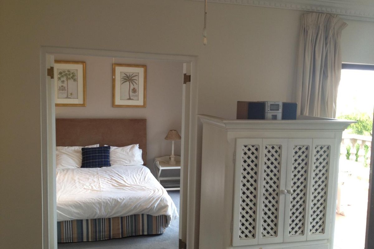 View from a living area looking into a bedroom with access to a balcony, featuring neutral wall finishes and classic crown molding.