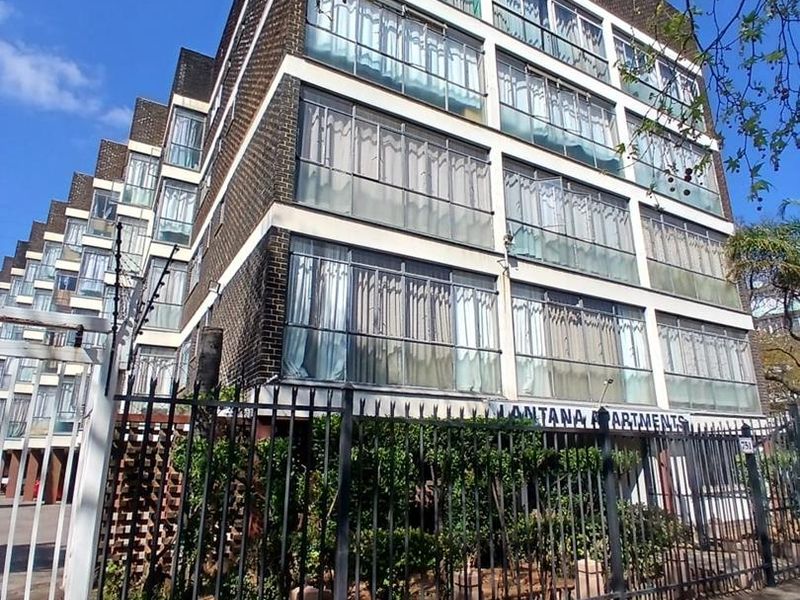 Exterior view of Lantana Apartments, featuring a multi-story brick building with enclosed balconies and secure perimeter fencing.