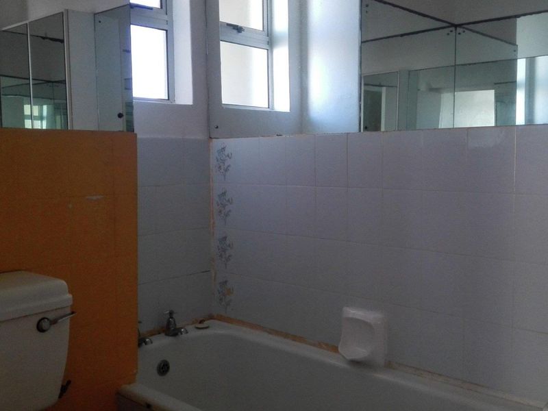 A dated bathroom featuring a standard bathtub, toilet, and wall-mounted mirrors, requiring cosmetic updates and tile repairs to modernize the space.