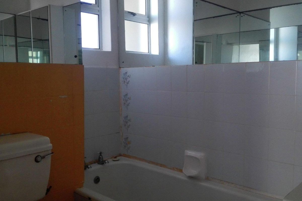 A dated bathroom featuring a standard bathtub, toilet, and wall-mounted mirrors, requiring cosmetic updates and tile repairs to modernize the space.