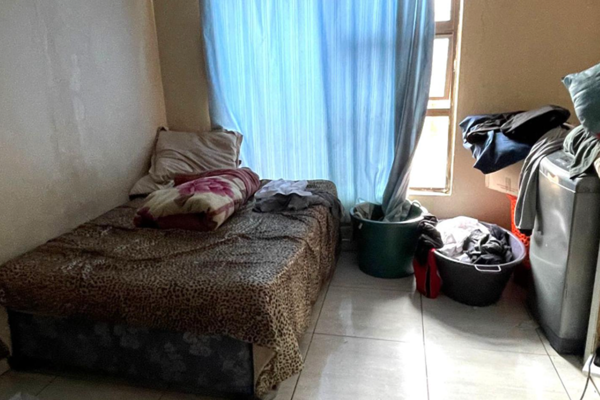A compact bedroom featuring tiled flooring and a window with curtains, providing a functional living space.