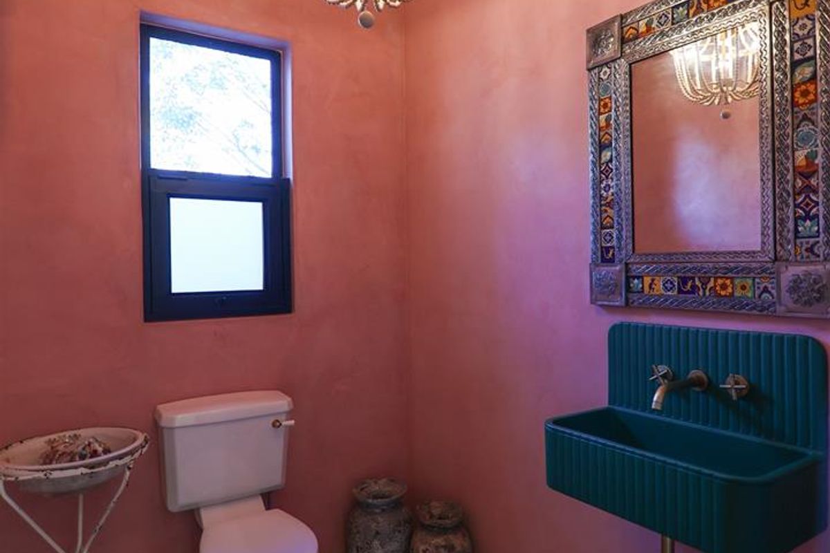 A unique powder room featuring a vibrant pink wall finish, a wall-mounted green basin, a decorative mirror, and a classic black and white checkered floor.