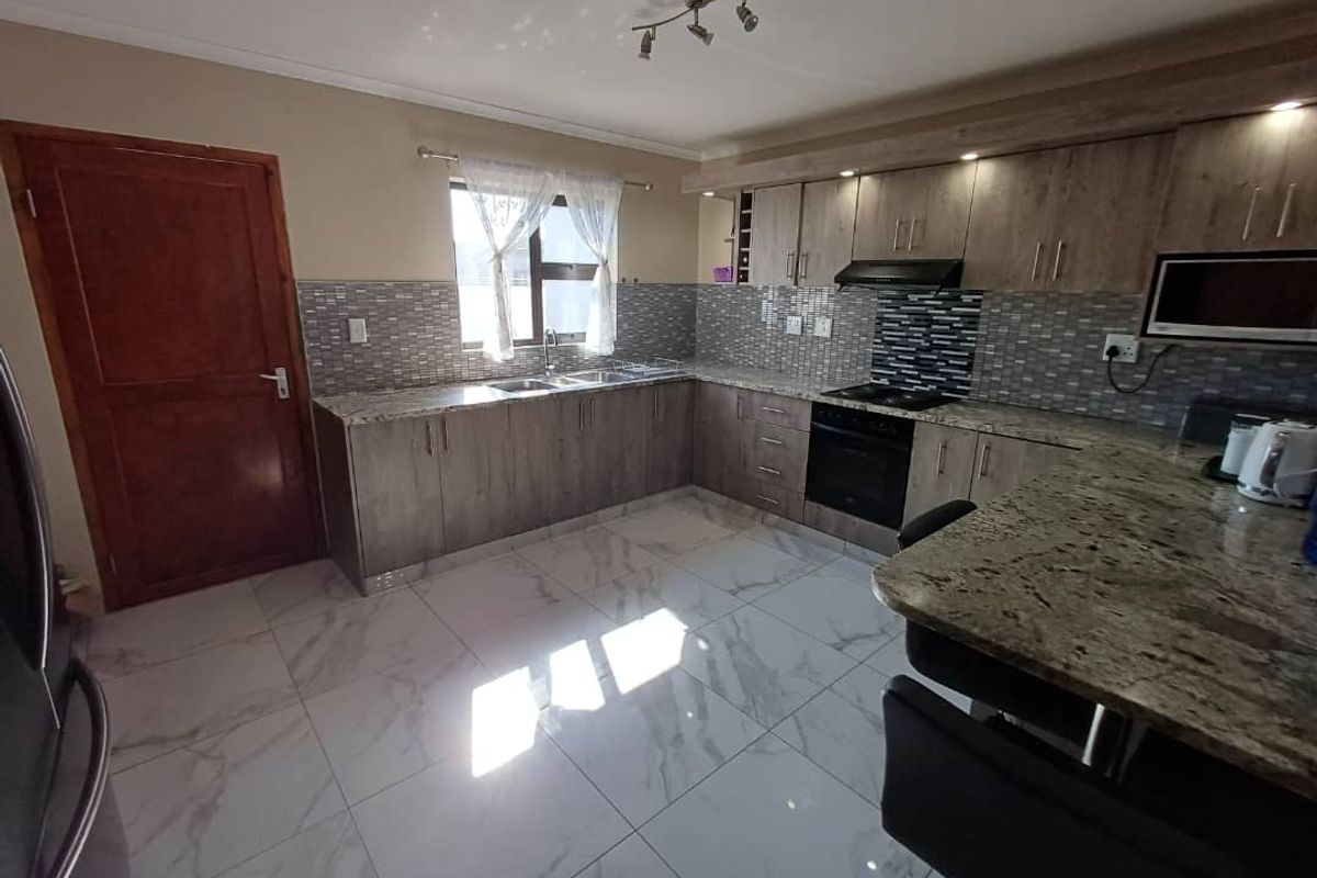 Modern kitchen featuring granite countertops, tiled backsplash, built-in oven and hob, and sleek cabinetry with a breakfast bar island.