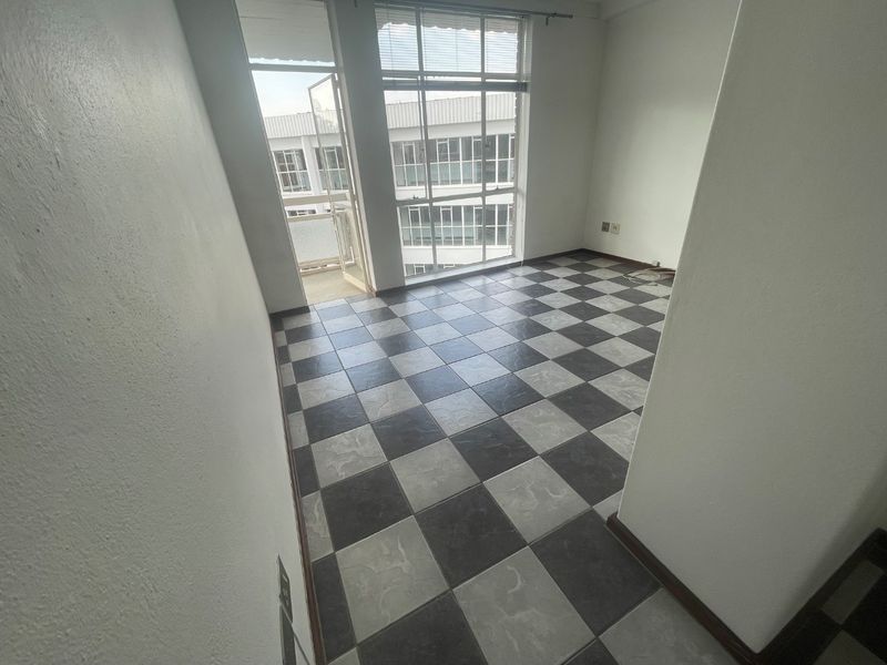 An empty living area featuring distinctive checkerboard floor tiles, large windows for natural light, and direct access to a balcony.