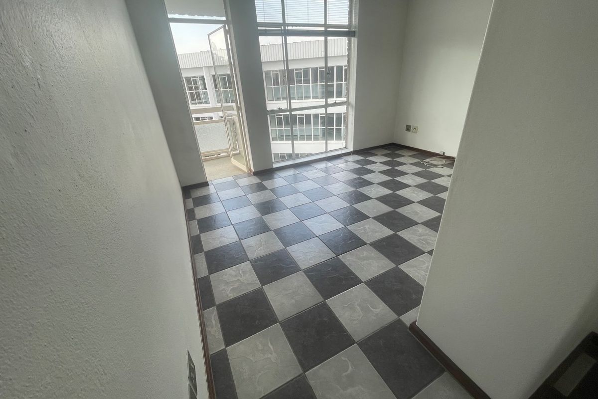 An empty living area featuring distinctive checkerboard floor tiles, large windows for natural light, and direct access to a balcony.
