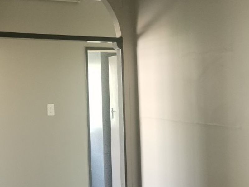 An empty hallway featuring an arched doorway, ceiling fan, and vinyl flooring, showing signs of wear and requiring cosmetic updates.