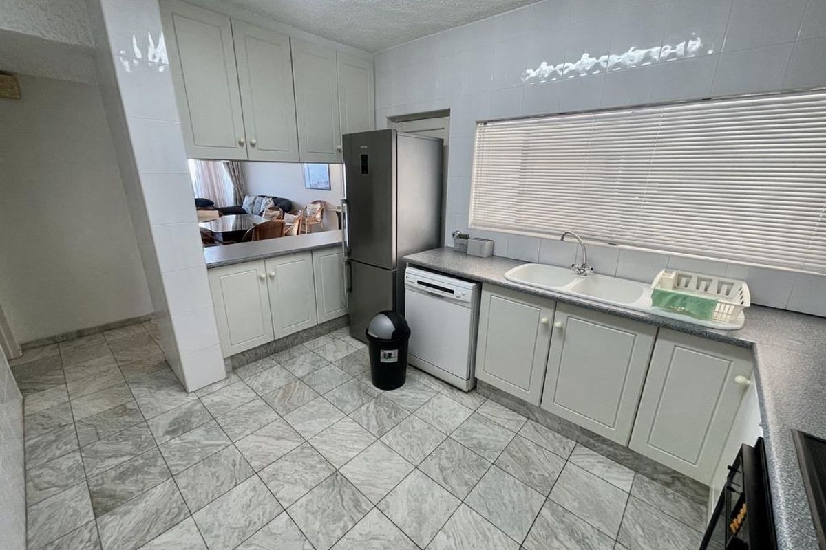 A functional kitchen featuring light-toned cabinetry, tiled flooring, a double basin sink, and a pass-through window connecting to the adjacent living area.