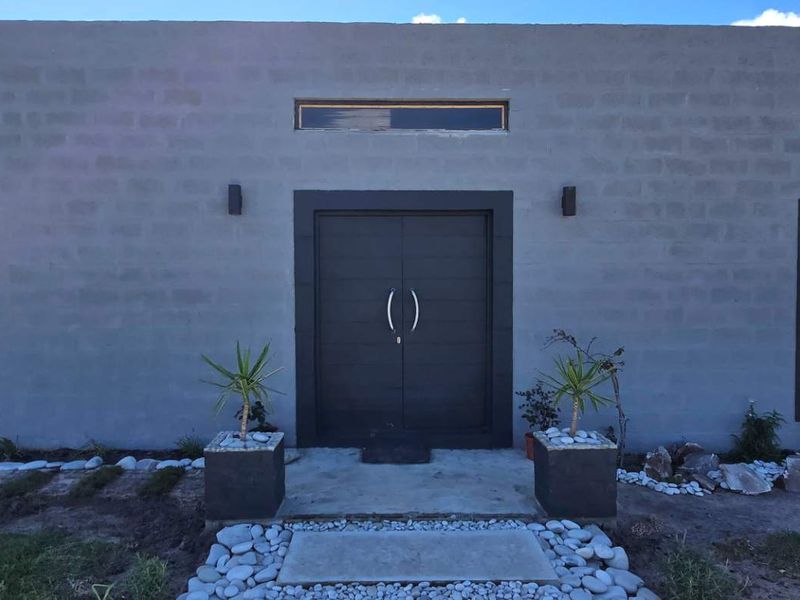 Modern single-story home facade featuring a grey concrete block finish, double front entrance doors, and large aluminium-framed windows.