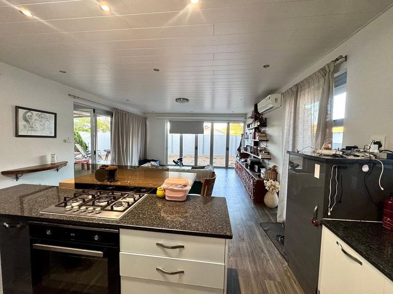 Spacious open-plan kitchen and living area featuring granite countertops, a gas hob, built-in oven, and direct access to the rear patio through sliding doors.