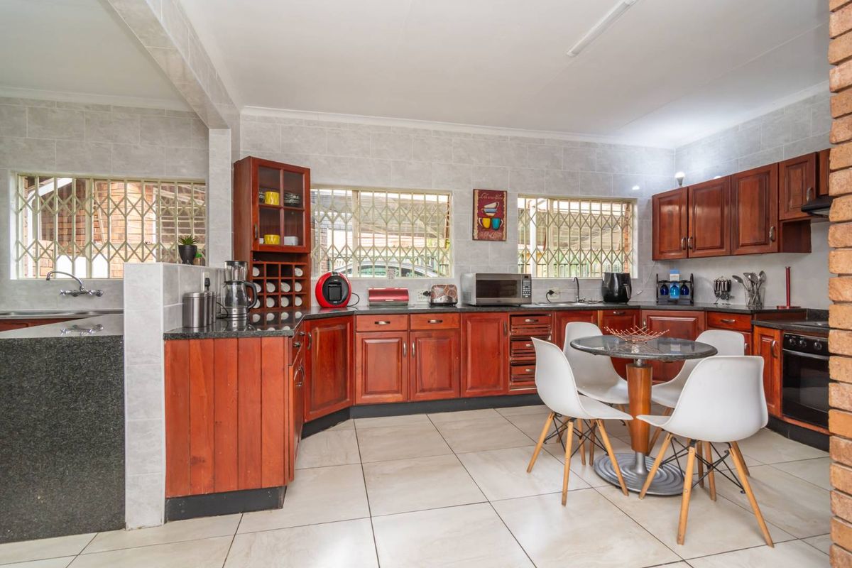 A functional kitchen featuring dark wood cabinetry, granite countertops, tiled flooring, and security bars on the windows.
