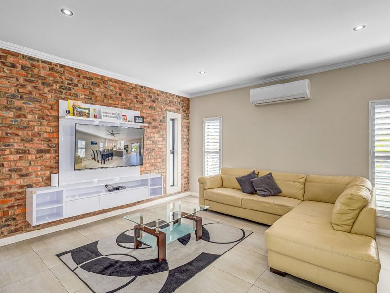 Spacious living room featuring an exposed brick feature wall, built-in media cabinetry, split-system air conditioning, and modern tiled flooring.