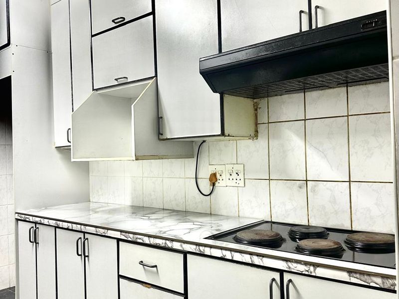 A functional kitchen featuring white built-in cabinetry, a marble-effect laminate countertop, an electric hob with extractor fan, and tiled backsplash and flooring.