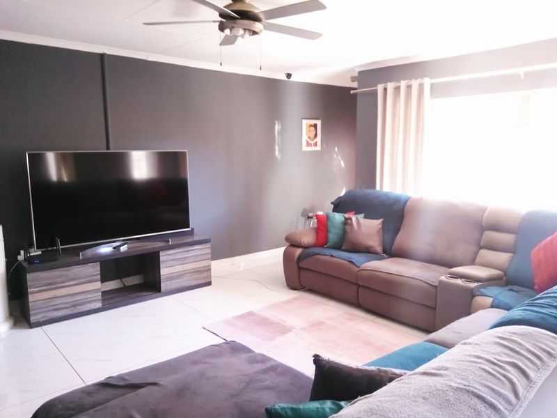 A comfortable living room featuring tiled flooring, a ceiling fan, and large windows with curtain rails, providing a bright and functional space.