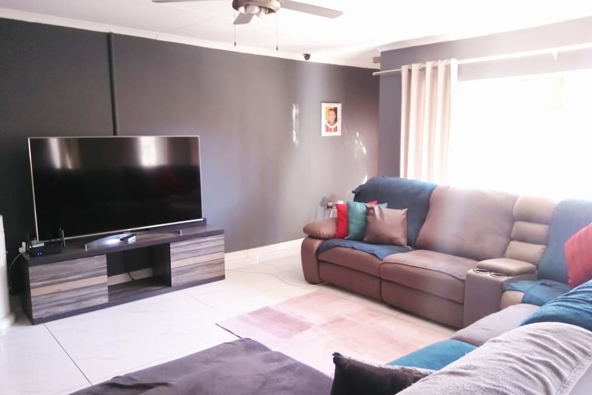 A comfortable living room featuring tiled flooring, a ceiling fan, and large windows with curtain rails, providing a bright and functional space.