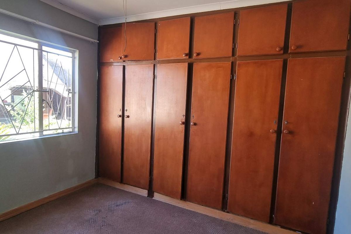 A bedroom featuring extensive built-in wooden cabinetry and a large window with security bars, providing ample storage space.