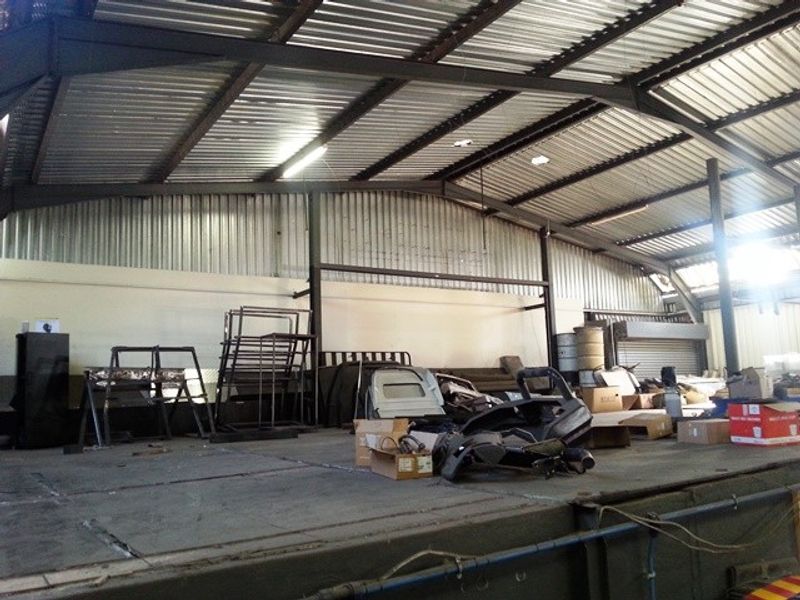 Spacious industrial utility area featuring a high corrugated metal roof, exposed steel structural beams, and a raised concrete platform suitable for storage or operations.