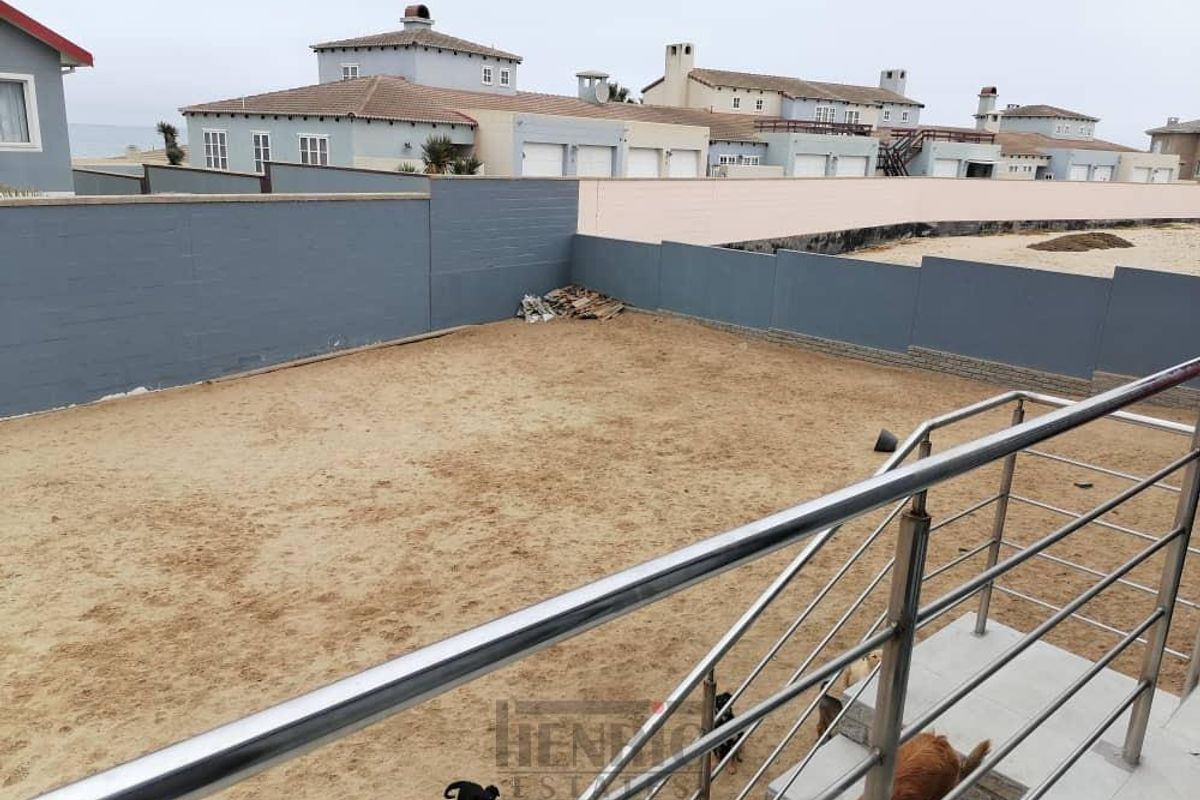 A view of a large, undeveloped sandy backyard area enclosed by perimeter boundary walls, viewed from an elevated balcony with stainless steel railings.