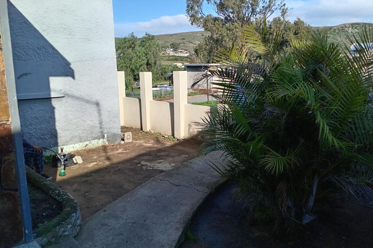 An outdoor side yard area featuring a concrete pathway, perimeter boundary wall, and established landscaping with views of the surrounding neighborhood.