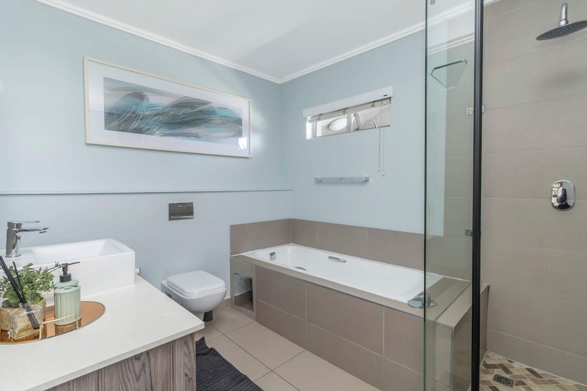 Modern bathroom featuring a built-in vanity, wall-mounted toilet, tiled bathtub, and a separate glass-enclosed shower with a rain shower head.