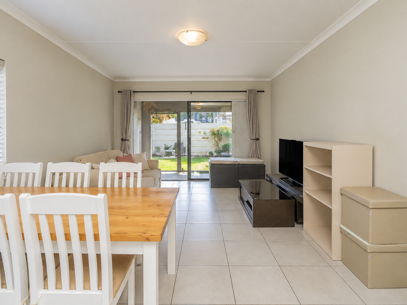 Open-plan living and dining area featuring neutral tiled flooring, coved cornicing, and a large sliding glass door providing direct access to the rear patio.