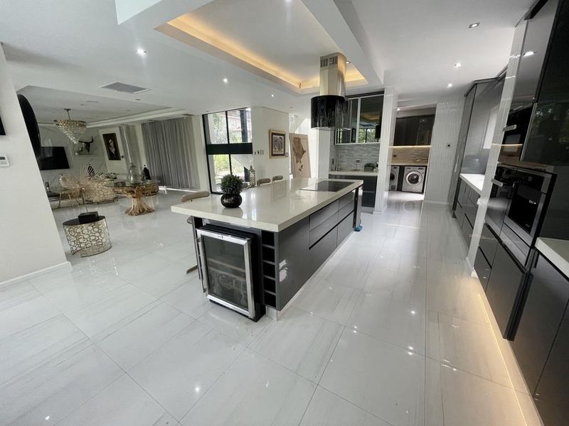 Modern open-plan kitchen featuring a large central island with quartz countertops, integrated appliances, sleek cabinetry, and polished tile flooring, flowing into the living area.