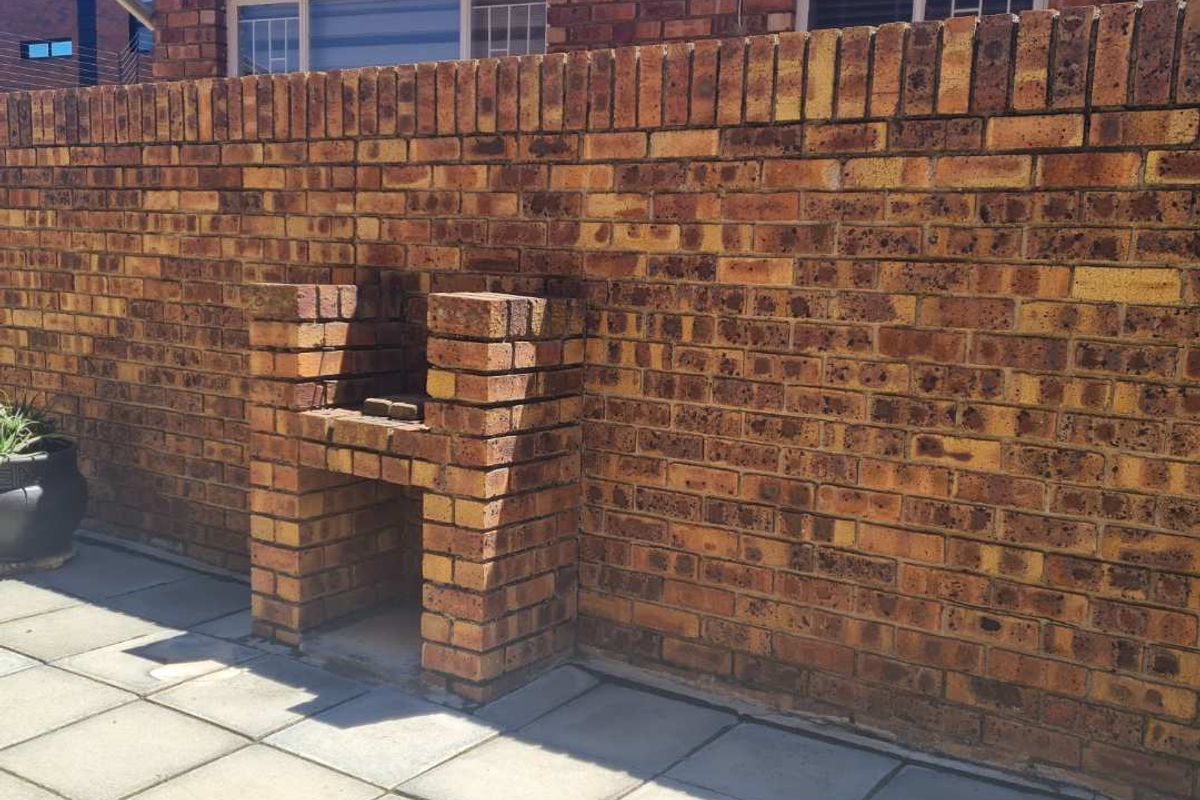 A private rear patio area featuring a built-in brick braai, paved flooring, and a brick boundary wall, offering a functional outdoor entertainment space.