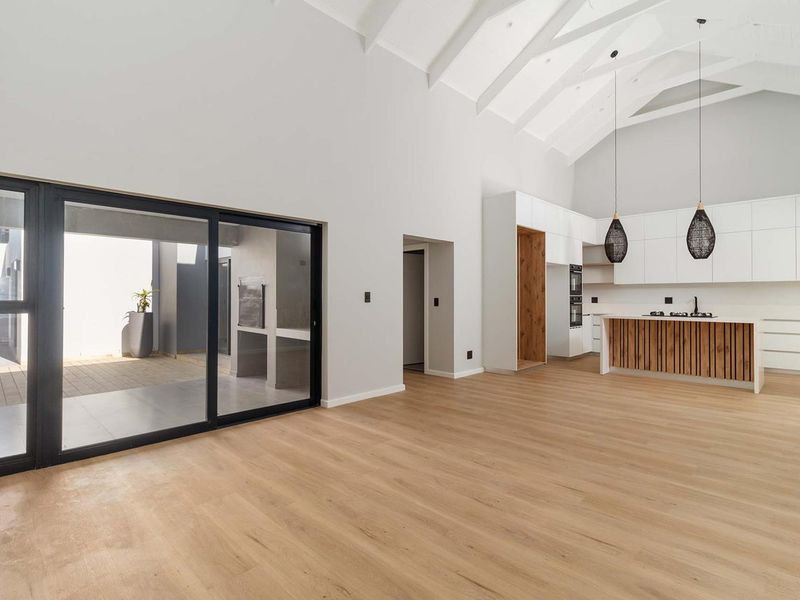 Spacious open-plan living area featuring a modern kitchen with island, vaulted ceilings with exposed rafters, and large sliding doors leading to an outdoor patio.