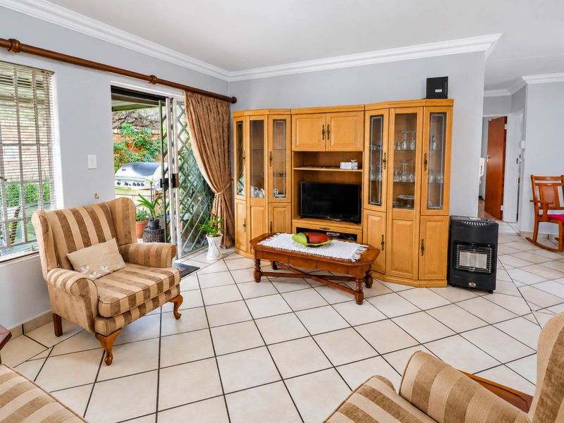 A bright living room featuring ceramic tile flooring, crown molding, and a sliding glass door providing access to the outdoor patio area.