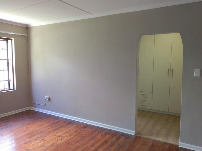 An empty bedroom featuring timber flooring, built-in cupboards, and a window with security bars.