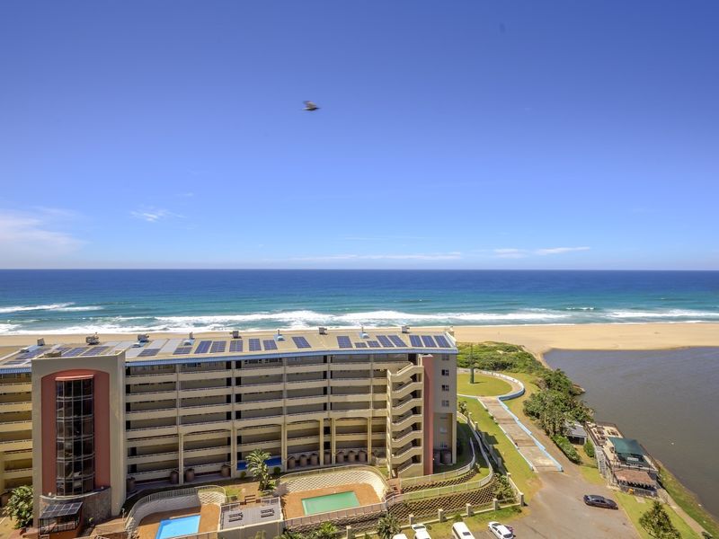 Aerial view of a beachfront apartment complex featuring solar panels, swimming pools, and direct access to the coastline and river estuary.