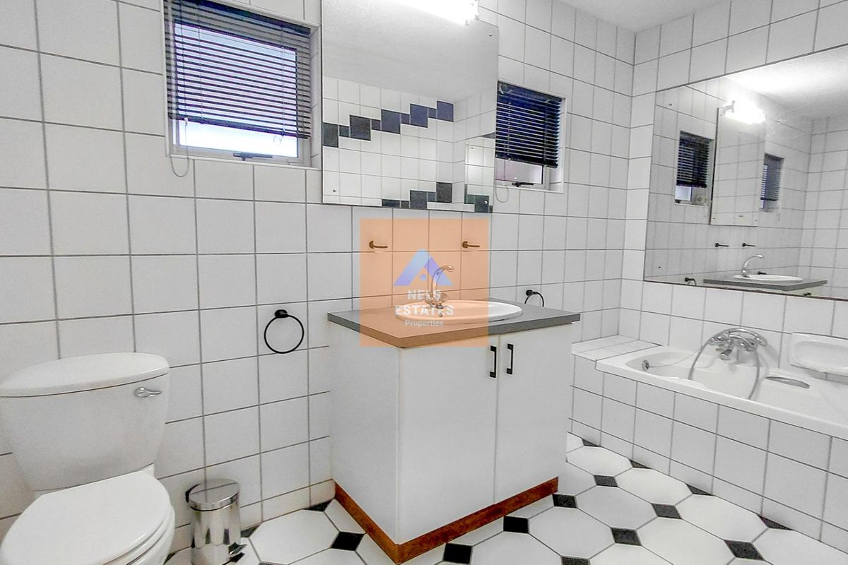 A functional bathroom featuring a vanity with basin, toilet, and bathtub, finished with classic white wall tiles and a patterned floor.