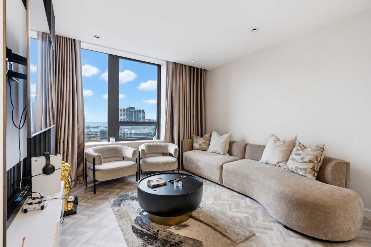 Modern living room featuring high-quality herringbone timber flooring, recessed lighting, and a large window offering expansive city and coastal views.
