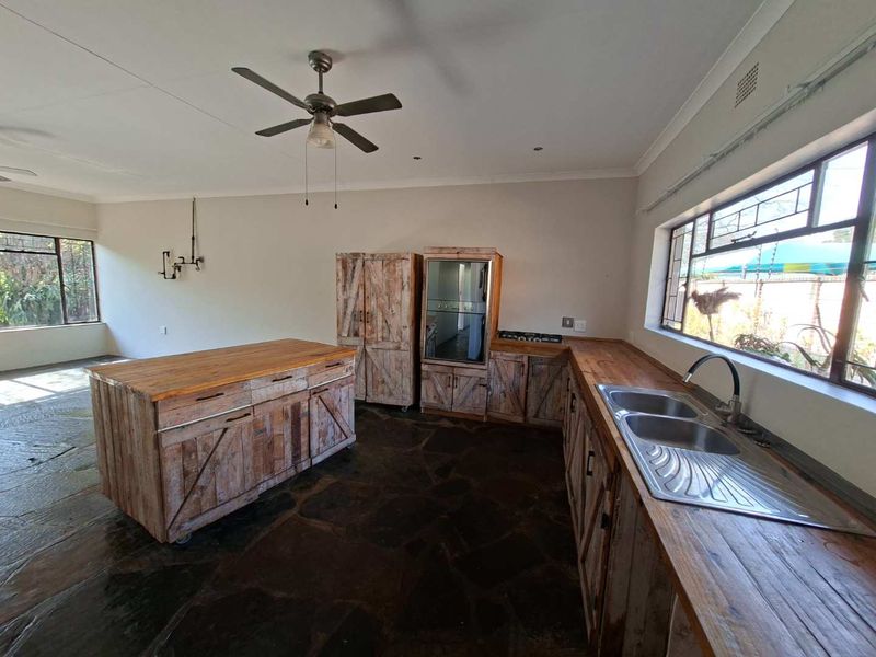 Kitchen featuring rustic wooden cabinetry, built-in oven, gas hob, double bowl sink, and stone flooring, offering a unique, textured aesthetic.