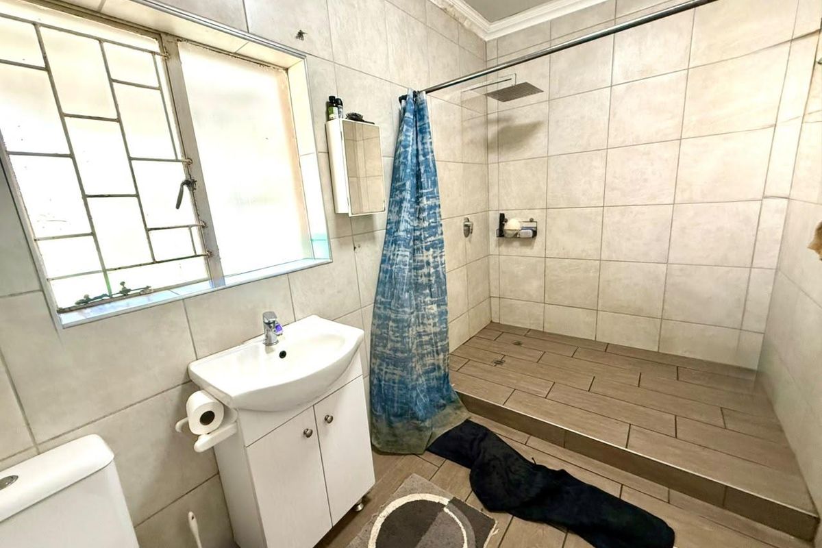 A functional bathroom featuring a walk-in shower, vanity basin, and toilet with neutral wall and floor tiling.