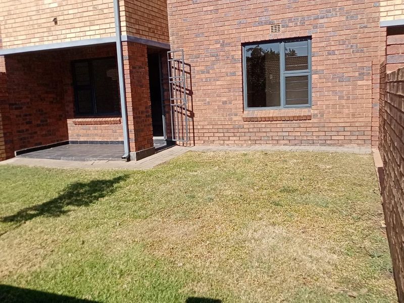 A private rear garden area featuring a paved patio, brick facade, and secure access gate, providing a functional outdoor space for the townhouse.