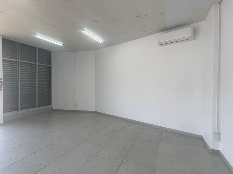 A clean, vacant retail or office space featuring tiled flooring, a suspended ceiling, and a wall-mounted air conditioning unit.