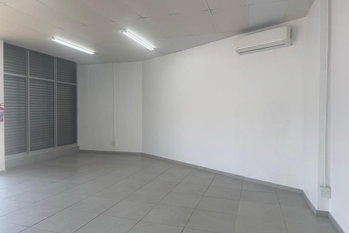 A clean, vacant retail or office space featuring tiled flooring, a suspended ceiling, and a wall-mounted air conditioning unit.