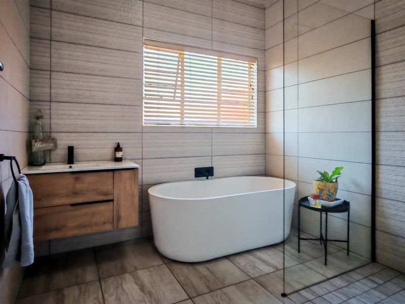 Modern bathroom featuring a sleek freestanding bathtub, wall-mounted vanity, glass shower screen, and contemporary tiled finishes with matte black hardware.