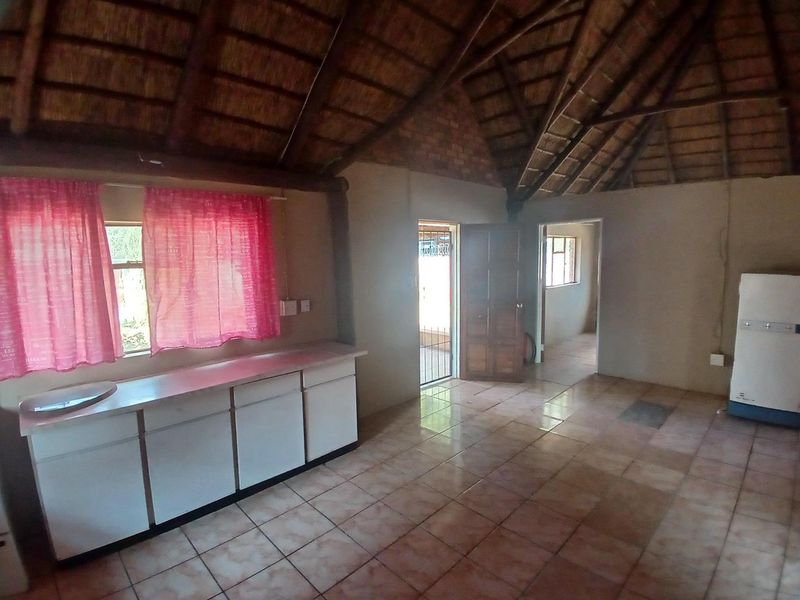 Open-plan living area featuring a traditional thatched roof with exposed rafters, tiled flooring, and basic built-in kitchen cabinetry.