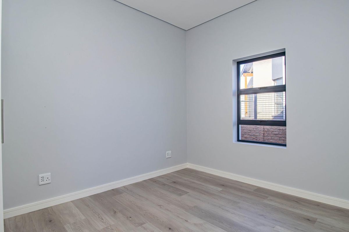 A bright, empty bedroom featuring modern light-toned wood-look flooring and a window with a view of the exterior.