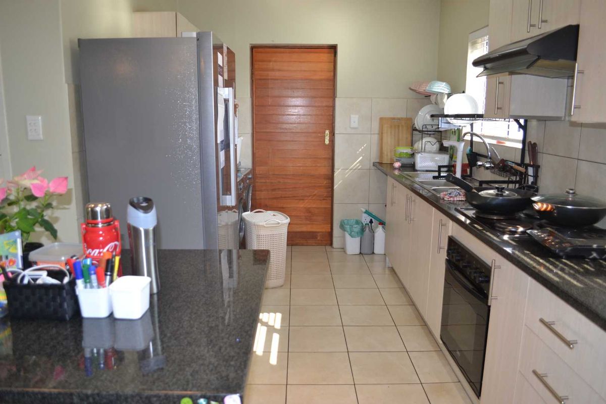 Functional kitchen featuring granite countertops, built-in cabinetry, integrated oven with extractor fan, and tiled flooring with direct access to a wooden door.