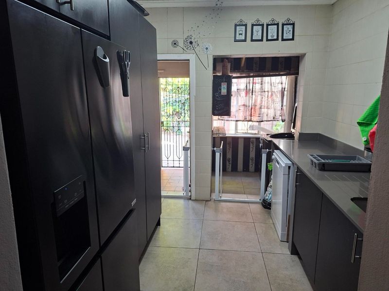 A functional kitchen featuring dark cabinetry, stone countertops, and tiled flooring, with direct access to an outdoor area through a security gate.