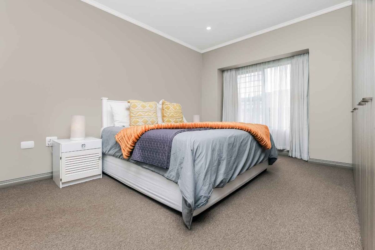 A well-maintained bedroom featuring neutral wall tones, plush carpeting, and built-in wardrobe storage with large windows allowing for natural light.